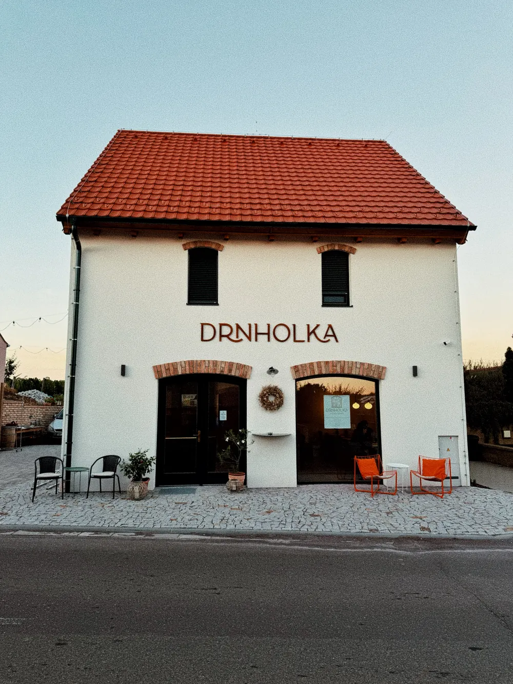 Vinný dům Drnholka ve Wolkerově ulici: bílá fasáda s cihlovými oblouky nad dveřmi, nápis DRNHOLKA a oranžová křesílka před vchodem