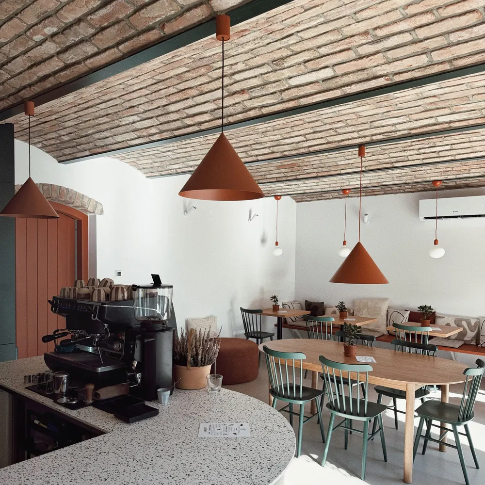 Espresso stroj na barovém pultu, v pozadí stoly pod klenutým stropem a oranžové lampy