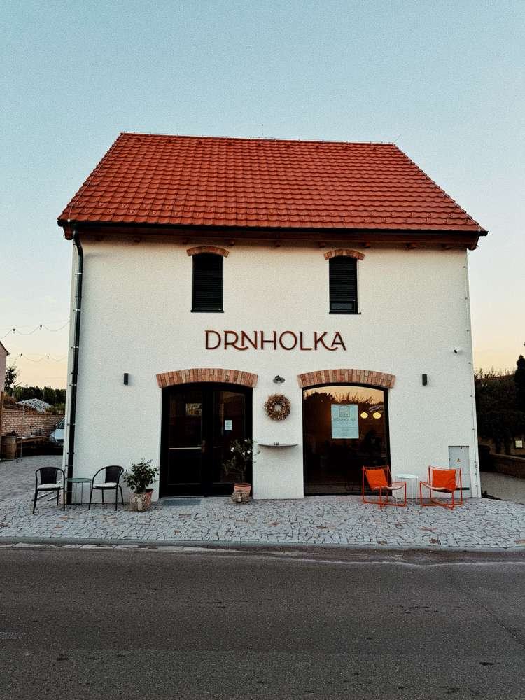 Vinný dům Drnholka dnes: bílá fasáda se zelenými dveřmi a cihlovými oblouky